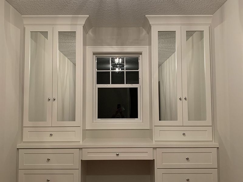 Floor to ceiling wardrobes with mirror doors flanking a window. 